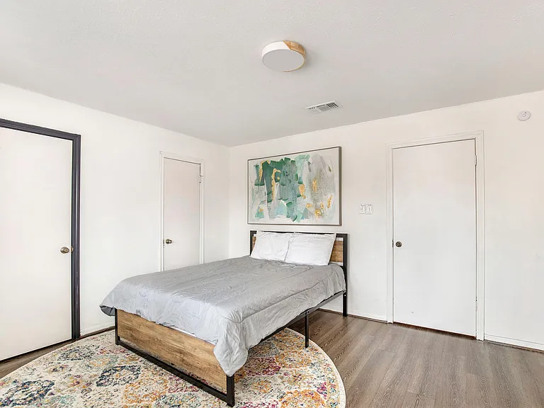 Spacious bedroom with a queen bed, wood-look flooring, and wall art, plus walk in closet.