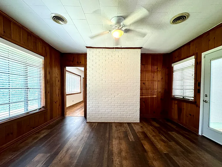 Den with original wood plank walls and new laminate flooring; door to driveway / back yard to the right.