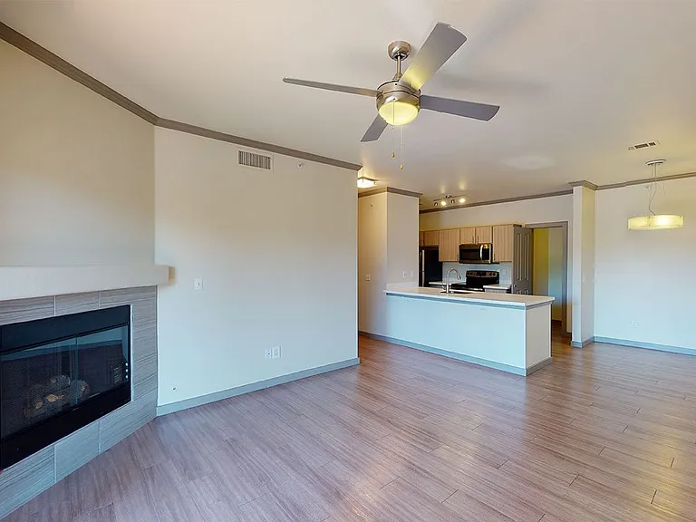 Apartment kitchen with stainless steel appliances, dining and living room with wood-style flooring.