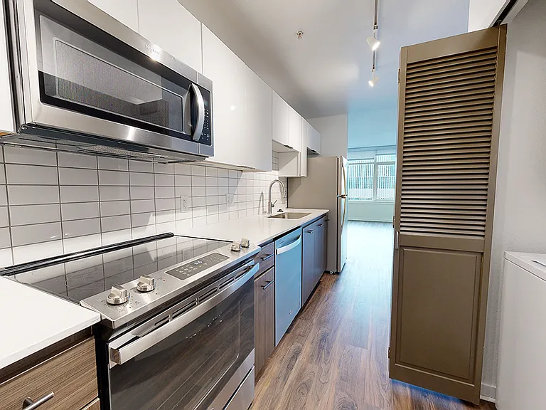 Apartment kitchen with stainless steel appliances, quartz countertops and wood-style flooring.