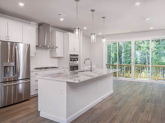 A modern, bright kitchen with white cabinets, stainless steel appliances, and a large window overloo