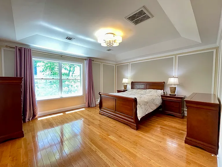 Spacious primary bedroom featuring tray ceiling, hardwood floors, and abundant natural light