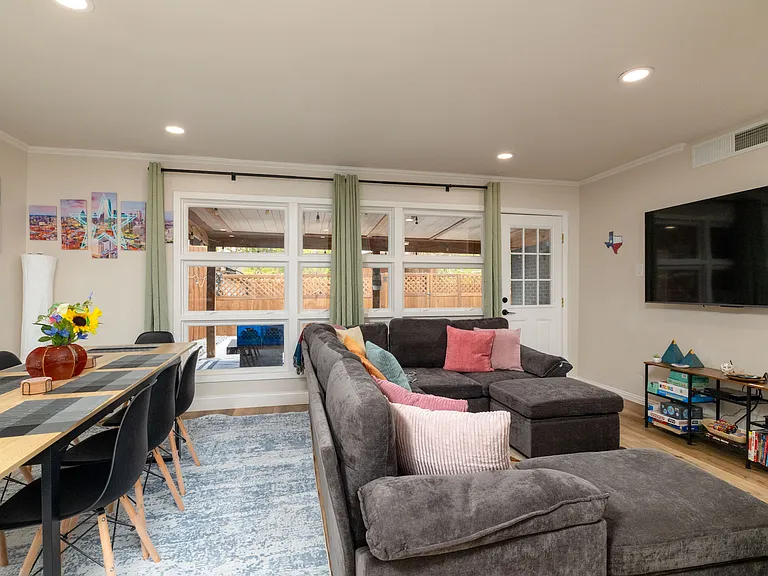 Bright, cozy living room with a large sectional, modern art, big windows, a smart TV, board games, and a DVD collection. Perfect for relaxing, gathering, or getting work done in a stylish, welcoming space.