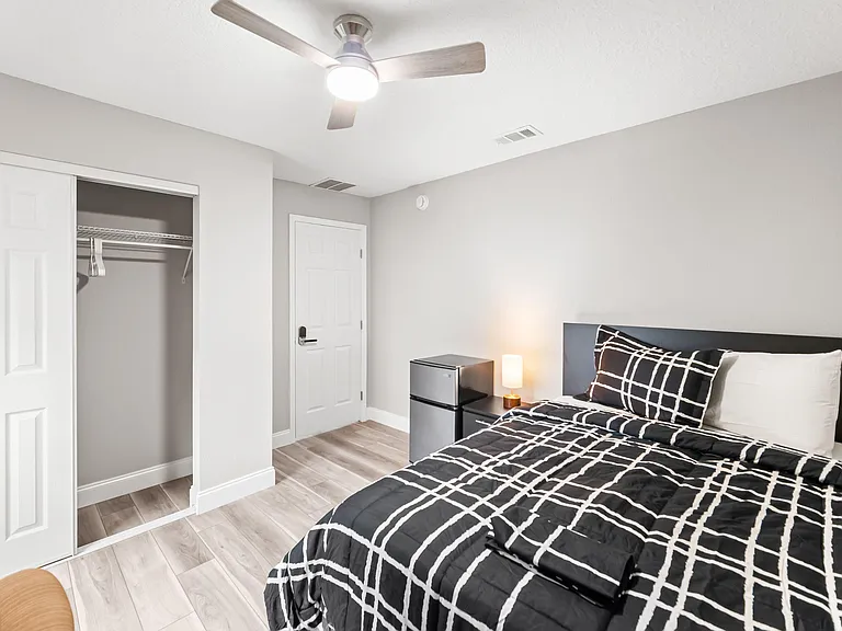 Private furnished bedroom with ceiling fan, closet storage, and a mini fridge with nightstand for added convenience.