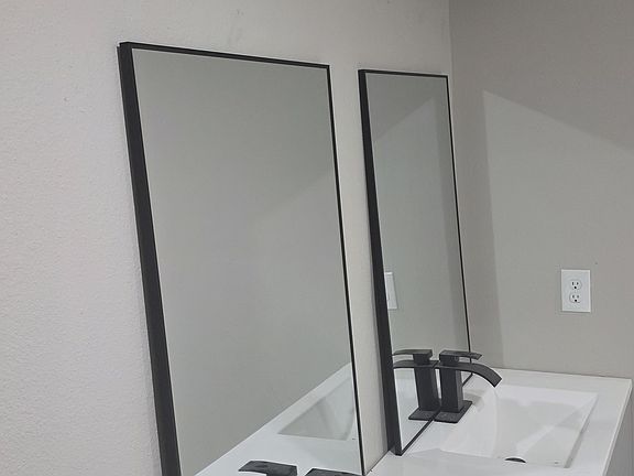 Primary bath double vanity with modern black lighting, black plumbing fixtures, and black framed mirrors