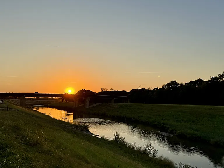 Riverside Walking Path with Bridge and Sunset Glow Near The Elm at River Park