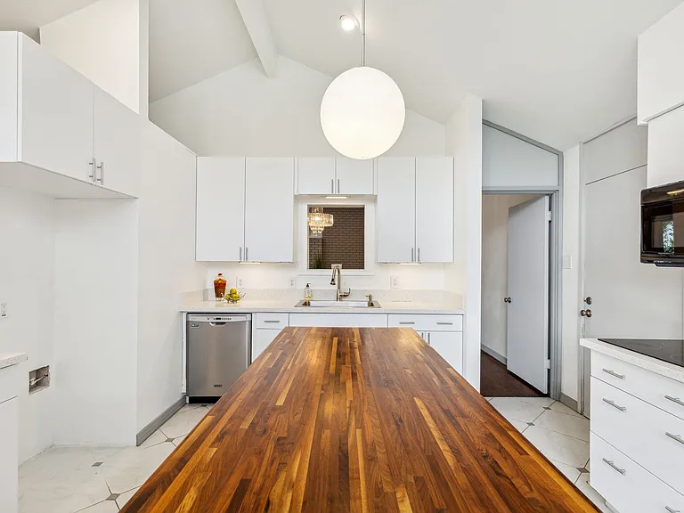 Kitchen featuring a butcher block island, white cabinetry, a stainless steel dishwasher, an over-range microwave, and vaulted ceilings