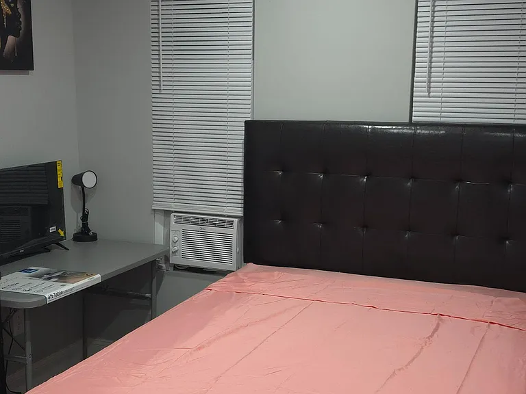 Furnished bedroom with a platform bed, two windows with blinds, and a convenient desk setup for work or study.