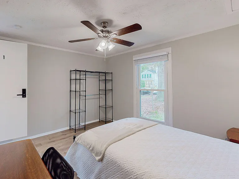 Furnished bedroom with ceiling fan, large window, and convenient open shelving plus a small desk/work area.