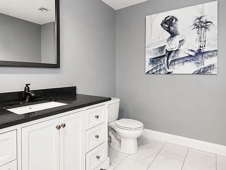 Updated bathroom with a granite-top vanity, ample cabinet storage, and sleek tile flooring for easy upkeep.