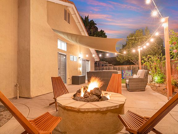 The fully fenced corner lot backyard is a charming retreat with a landscaped garden, a cozy fire pit, and a patio set for gatherings. Twinkling patio lights and a sunshade sail add ambiance and comfort, making it perfect for outdoor relaxation.