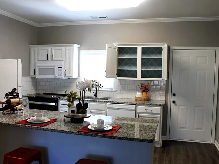 Kitchen - white cabinetry, appliances, granite countertop, kitchen bar, sink & access to patio.