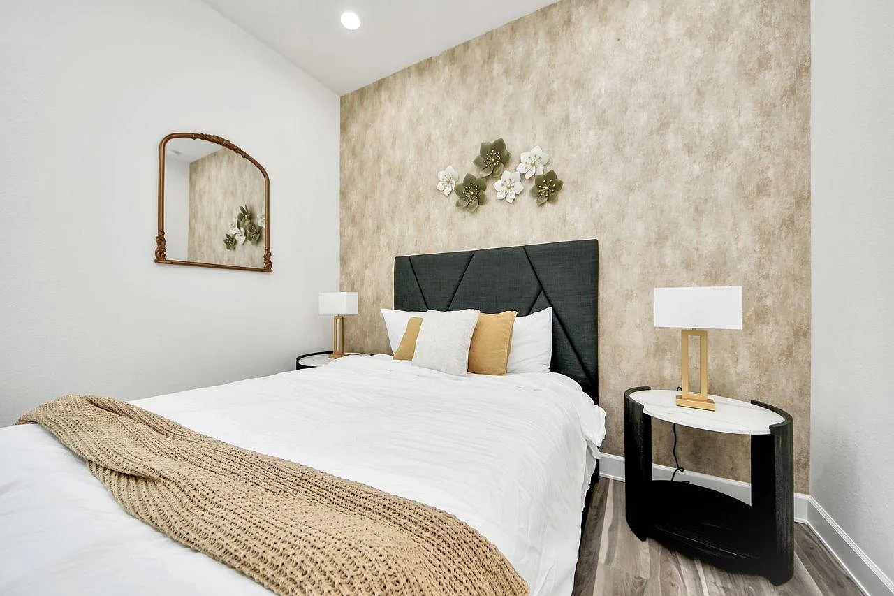 Staged bedroom with a double bed, padded headboard, two nightstands with lamps, and an accent wall for added style.