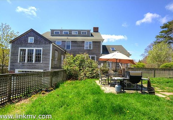 Back yard with stone dining patio, deck off the kitchen, and walk-out basement with barn-style doors.
