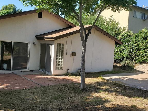 Backyard view of large brick patio and basketball hoop, taken from far corner standing on small brick patio.