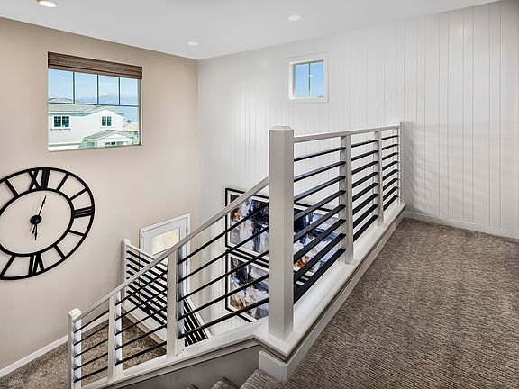 A modern staircase with a large clock on the wall, leading up to a second floor with a window overlo