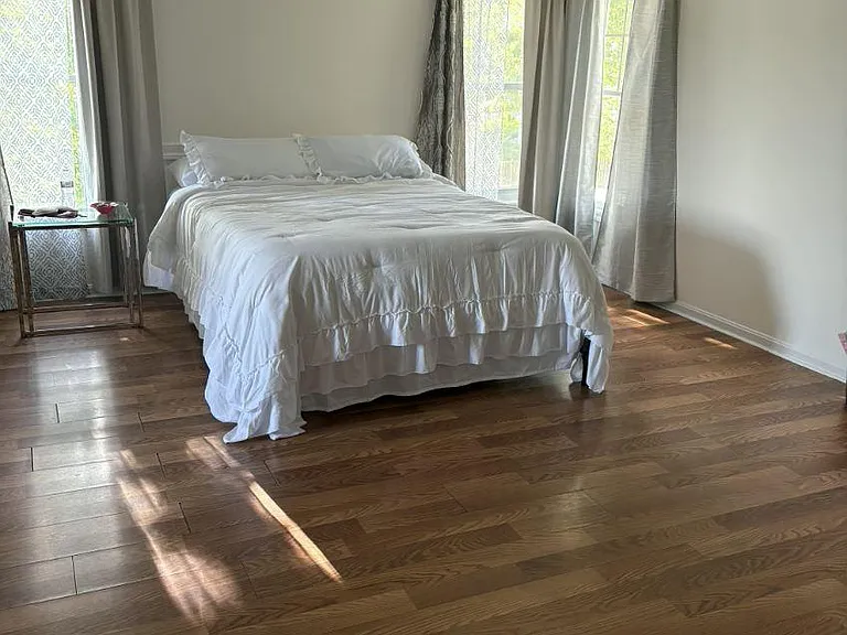Spacious bedroom with hardwood floors, ceiling fan, and multiple windows with curtains for privacy and natural light.