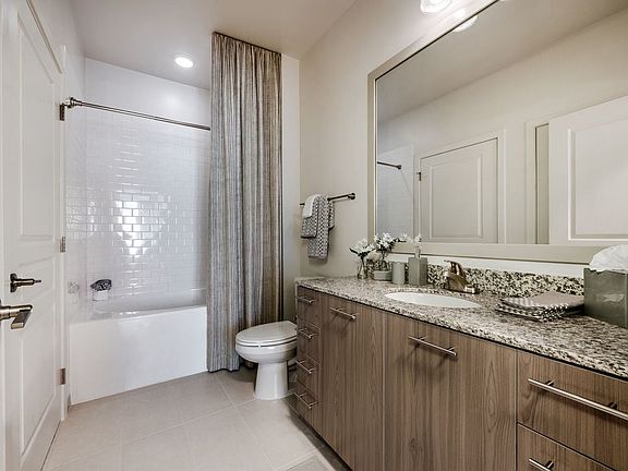 Bath with granite countertops, brown cabinetry, hard surface flooring and tiled bathtub