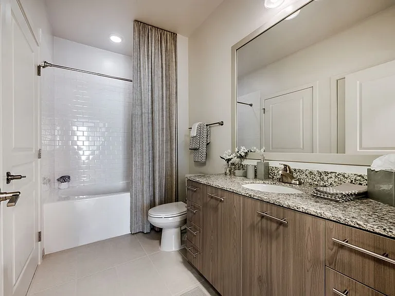 Bath with granite countertops, brown cabinetry, hard surface flooring and tiled bathtub