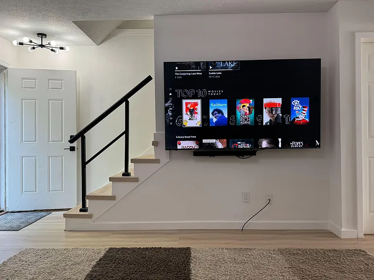 Open common area with a wall-mounted TV, updated lighting, and easy access to the stairway and entry hall.