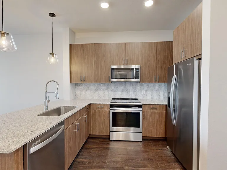 Apartment kitchen with stainless steel appliances, granite countertops, and wood-style flooring.
