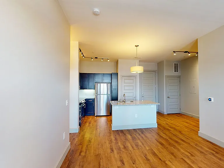 Apartment kitchen with stainless steel appliances, dining and living room with wood-style flooring.