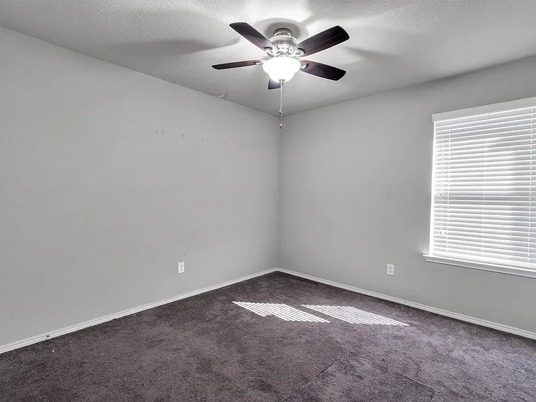 Bedroom featuring neutral gray walls, dark gray carpet, a white ceiling fan with light fixture, and a window with white blinds