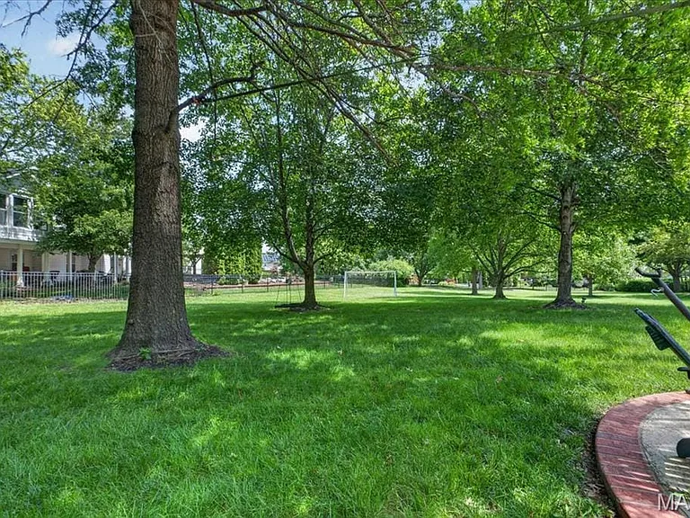 Expansive green lawn framed by mature trees, featuring a visible portion of a home with a columned porch and fencing