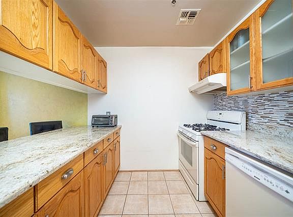 Bright galley kitchen with granite countertops, ample wood cabinetry, tile backsplash, gas stove, and dishwasher. Functional layout with plenty of light and seamless flow to the dining area.