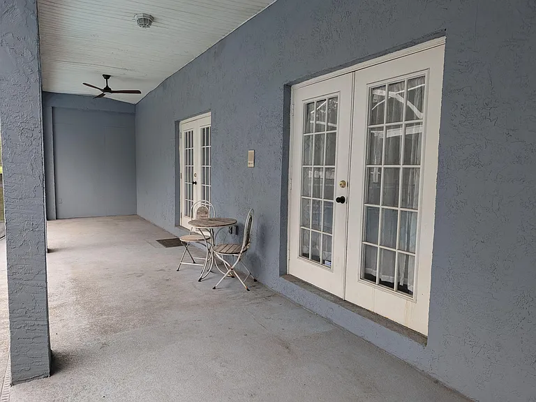 Covered patio with ceiling fan and French-door access, plus space for a small bistro set and outdoor seating.