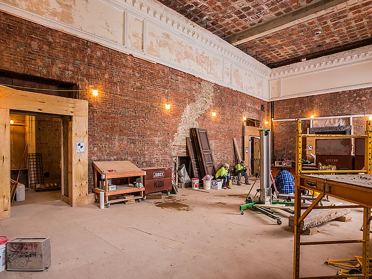Before: Large interior room during renovation showing tall ceiling, exposed brick and elegant crown molding