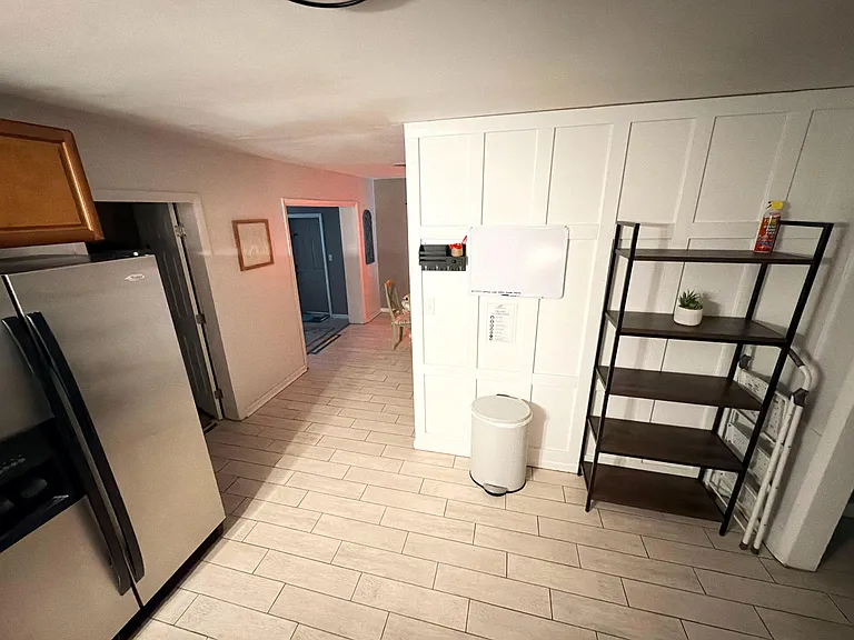 Galley kitchen with refrigerator, tile flooring, and open shelving for pantry storage, flowing into the adjacent hallway.