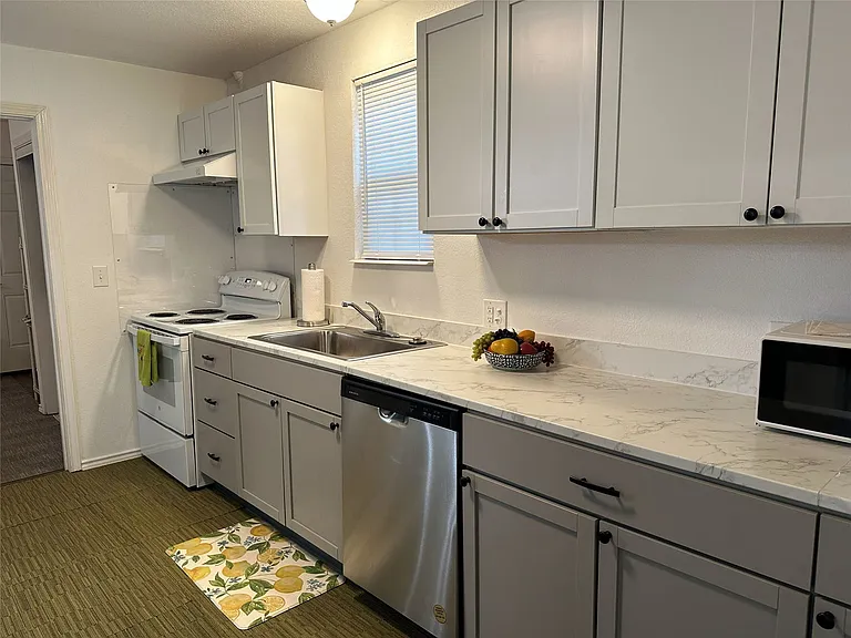 Kitchen featuring light gray cabinetry with black hardware, white countertops, stainless steel dishwasher, and a white electric range with a coordinating range hood