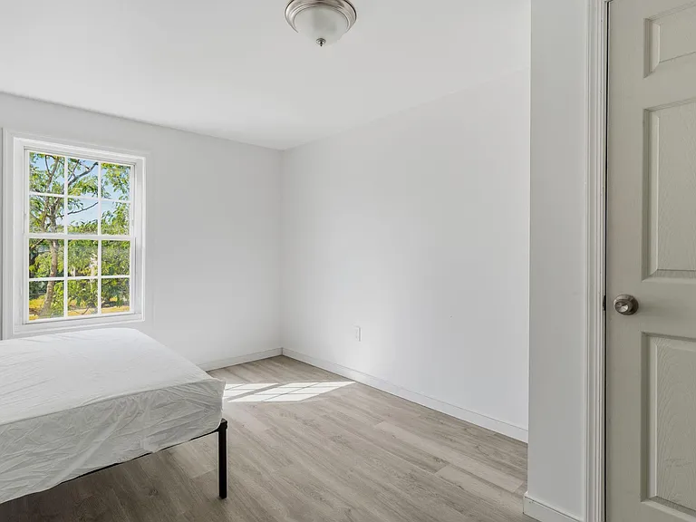 Bedroom with a large window, neutral finishes, and durable wood-look flooringan easy setup for a bed and essentials.