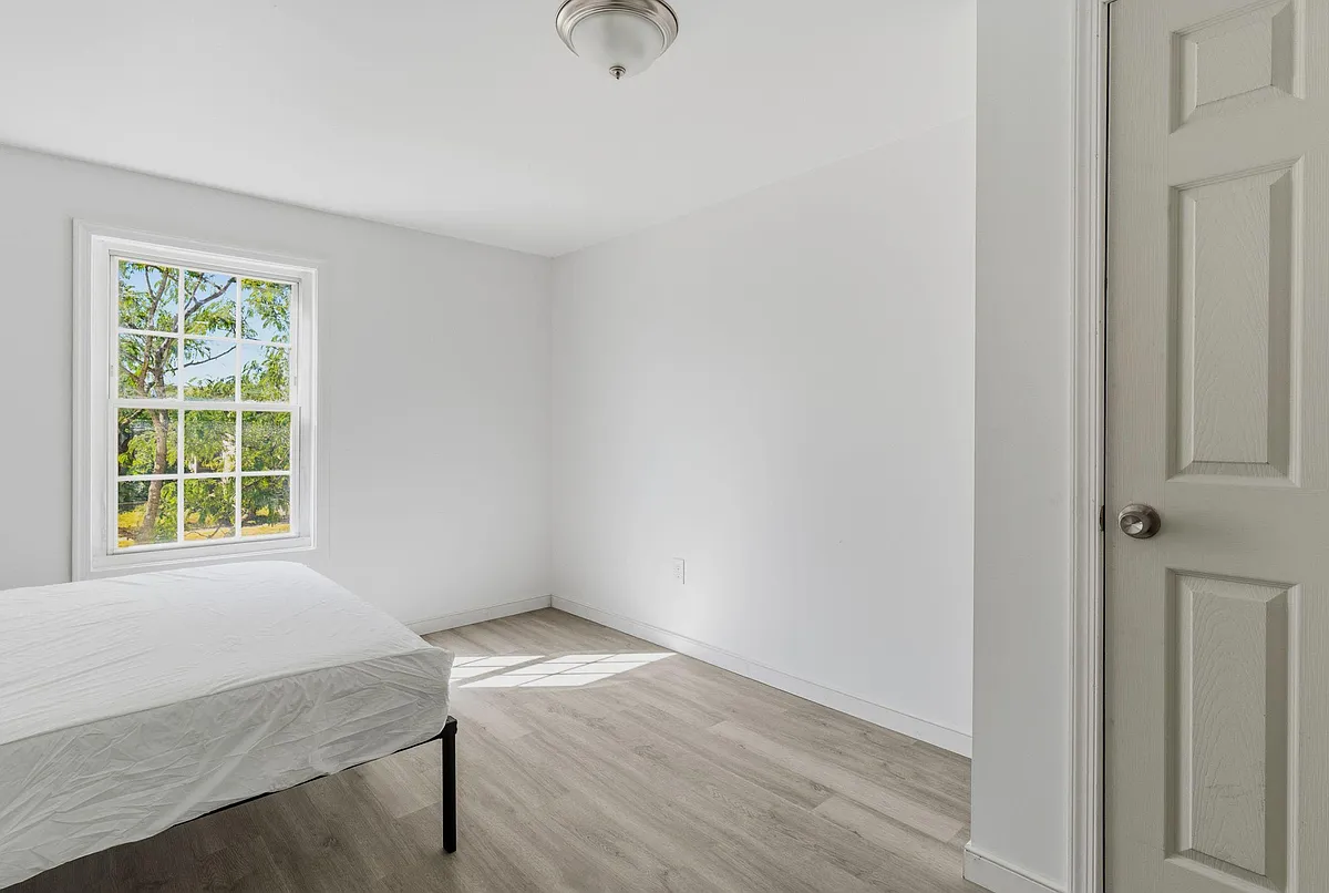 Bedroom with a large window, neutral finishes, and durable wood-look flooringan easy setup for a bed and essentials. - S South St