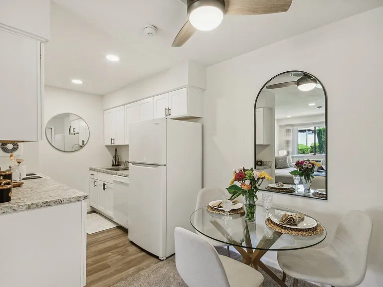a white kitchen with granite counter top and dining area with a glass table and chairs