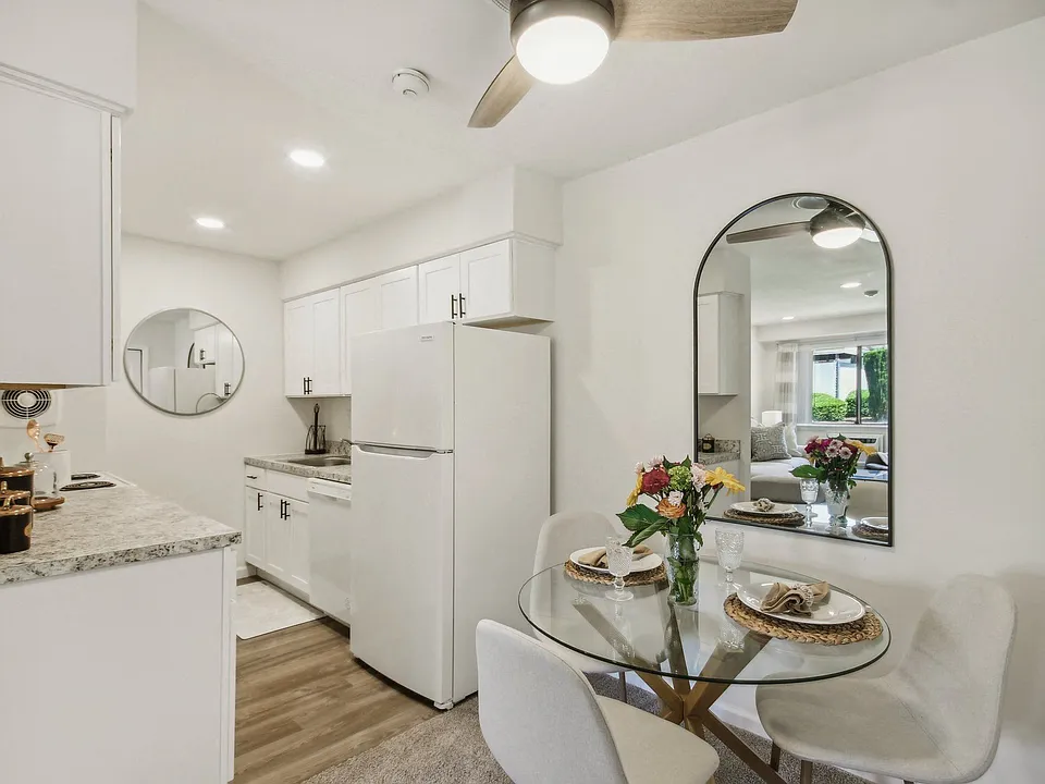 a white kitchen with granite counter top and dining area with a glass table and chairs