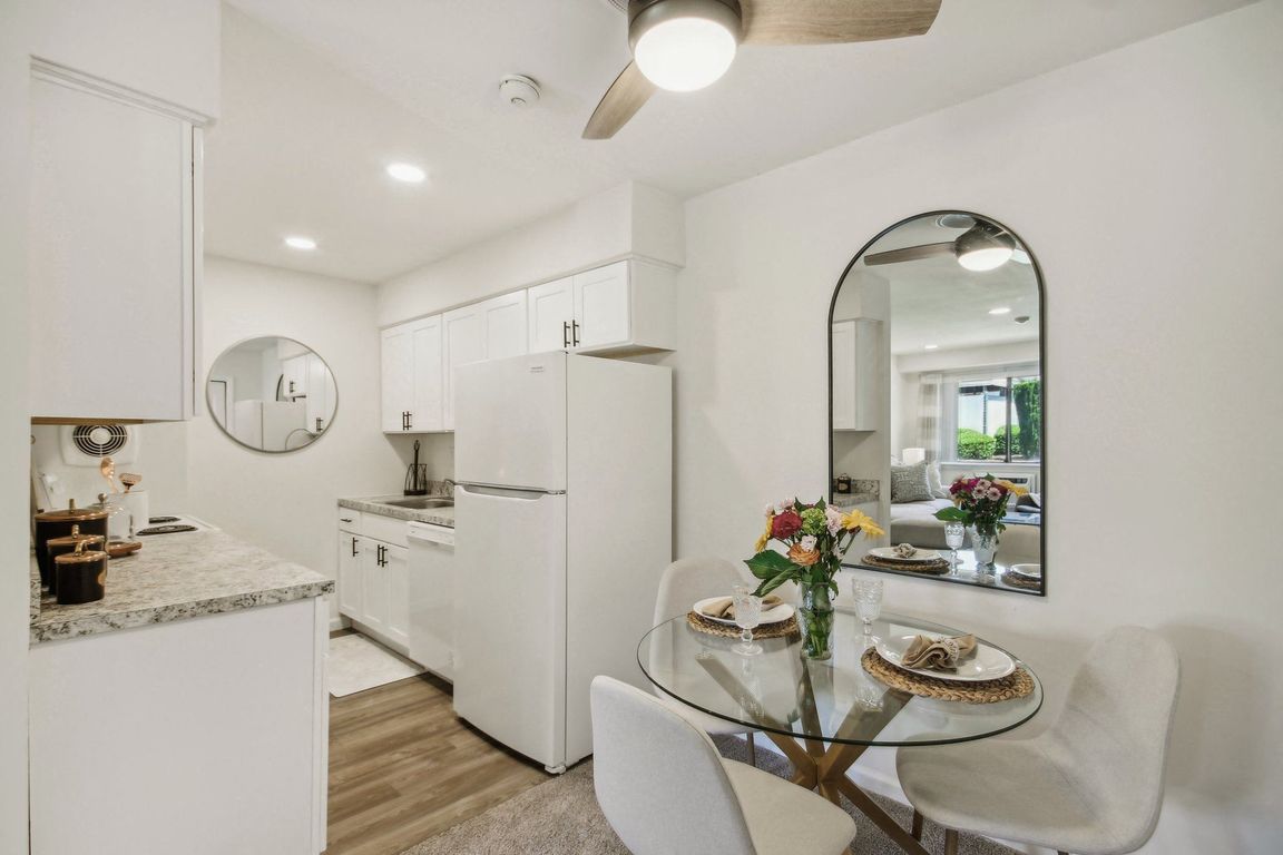 a white kitchen with granite counter top and dining area with a glass table and chairs