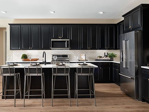 A modern, sleek kitchen with dark cabinets, stainless steel appliances, and a large island with bar