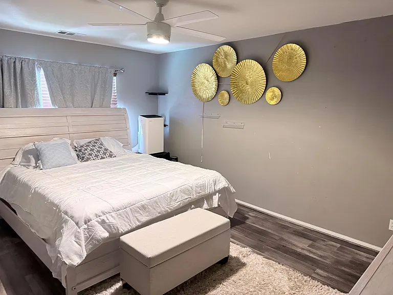 Furnished bedroom featuring a bed with headboard, ceiling fan, and window with curtains, plus a bench for extra seating.
