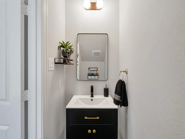 Modern vanity featuring a black cabinet with gold-tone hardware, a white integrated sink, and a black faucet