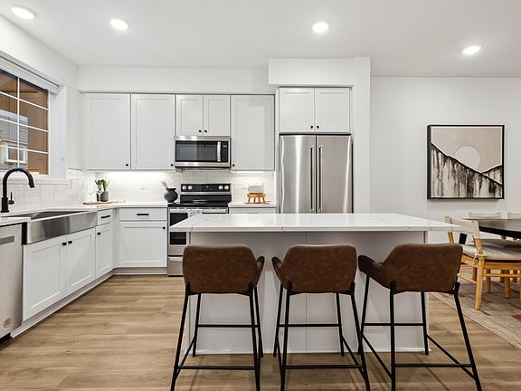 A modern, open-concept kitchen with white cabinets, stainless steel appliances, a large island with