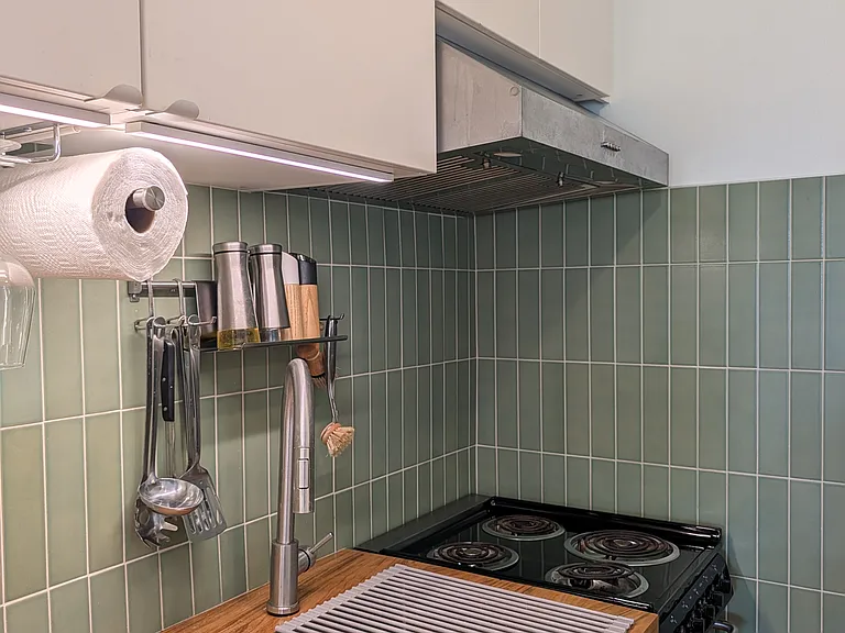 Compact kitchen with stainless steel sink and faucet, a range, exhaust fan, refrigerator, microwave and storage cabinets.