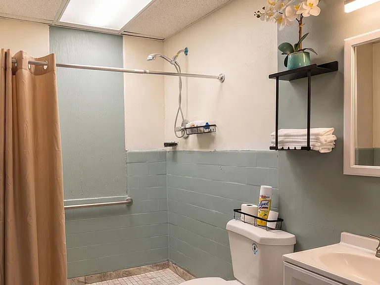 Clean bath with tiled shower, curtain rod, vanity sink, and wall shelving for towels and toiletries.