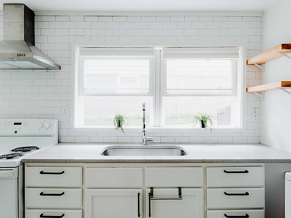 Kitchen windows let tons of light in! The kitchen has four custom open shelves, quartz countertop, a large stainless steel sink and a range hood!