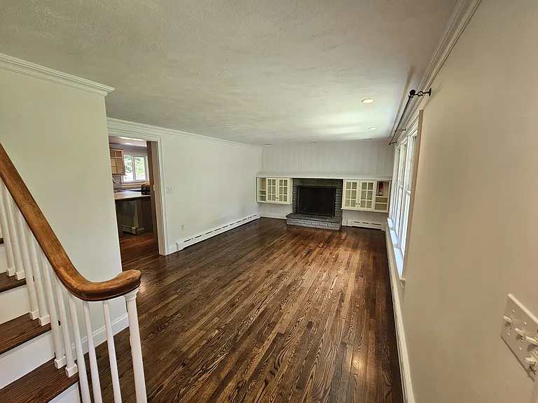 Spacious living room with hardwood floors, a wood-burning fireplace, built-in cabinetry, and natural light from the front-facing windows.