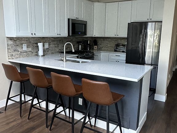 Open, modern kitchen with counter seating, stainless steel appliances, and stocked kitchen (dishware, silverware, pots/pans, glasses, wine glasses, pot/pans, etc.)