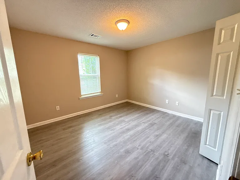 Bright second bedroom featuring a wide window, fresh paint, and seamless new flooring.