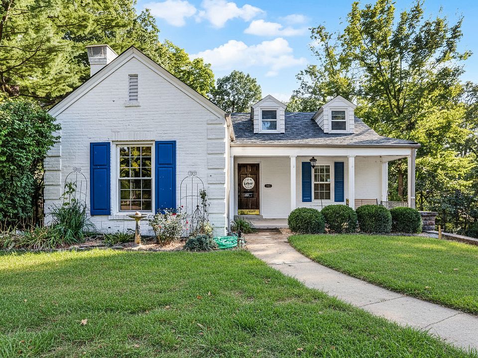 Charming white-brick cottage with bold blue shutters and an inviting front porch.
