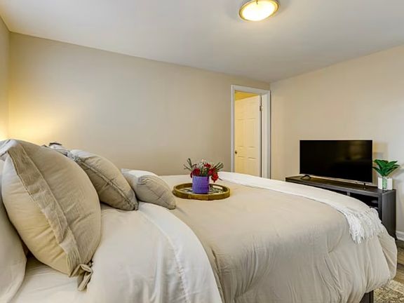 Stylish master suite with two bedside tables, flat-screen TV, and plenty of natural light _ fully furnished for comfort and convenience.
